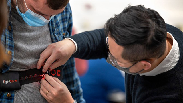 A researcher helping strap on a wearable sensor around a man's waist.